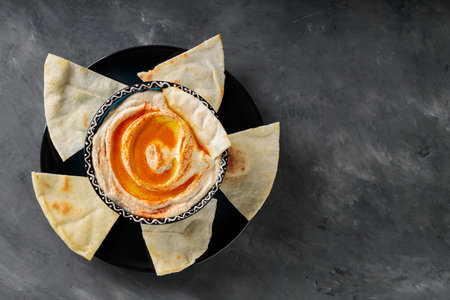 Chickpea Hummus with Pita Chips and Paprika on Dark Concrete Background, Top View, Copy Space
