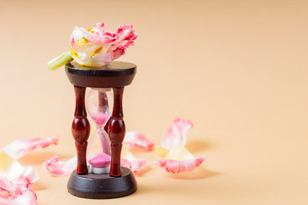 Hourglass and Fading Flower Petals on Beige Background, Concept of Urgency to Solve Environmental...