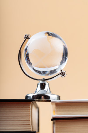 Glass Globe on Stack of Books on Beige Background, Fragile Balance of Earth's Ecosystemの写真素材