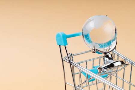 Shopping Cart with Glass Globe on Beige Background, World Trade Concept, Copy Spaceの写真素材