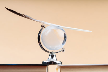Glass Globe with Balancing Bird Feather on Stack of Books, Fragile Balance of Earth's Ecosystem Conceptの写真素材