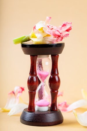 Hourglass and Fading Flower Petals on Beige Background, Concept of Worsening Environmental Problems,...