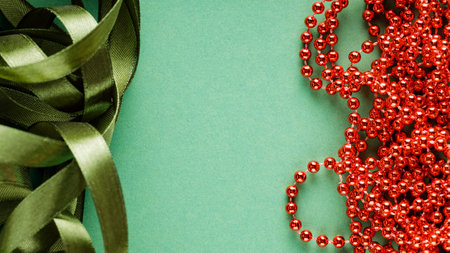 Green Festive Ribbon and Red Beads on Green Background, Christmas and New Year Decorations Concept, Copy Spaceの写真素材
