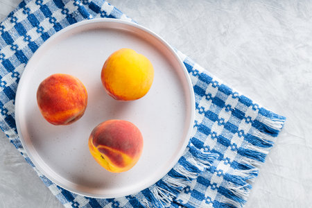 Ripe Peaches on White Plate with Linen Blue White Napkinの写真素材