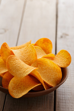Golden Potato Chips in Bowl on Rustic Wooden Surfaceの写真素材
