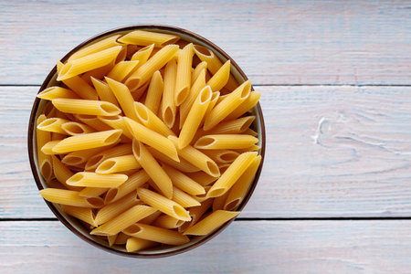 Dry Yellow Penne Pasta in Bowl on Wooden Background Top View Copy Spaceの写真素材