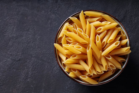 Dry Yellow Penne Paste in Ceramic Bowl on Dark Background