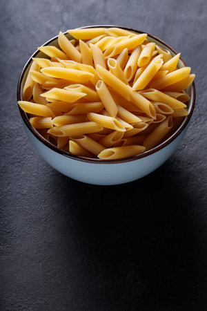 Dry Yellow Penne Paste in Ceramic Bowl on Dark Backgroundの写真素材