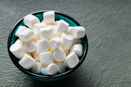 White Marshmallow Candies in Bowl on Green Background Copy Space