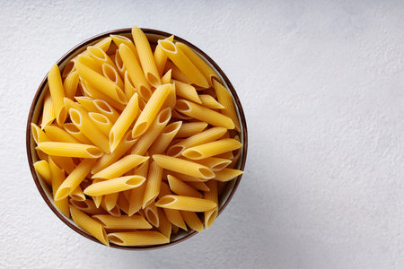 Uncooked Penne Paste in Ceramic Bowl on White Textured Backgroundの写真素材