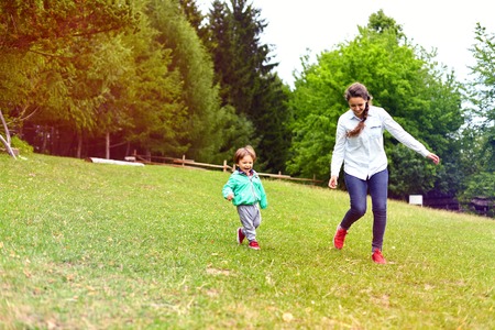 Young mother running with little boy on sunny day in the park.Mother and toddler in park having fun.Happy woman with adorable child.Motherhood and childhood concept, positive human emotions, feelings.の写真素材