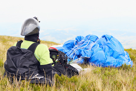 Paraglider with blue parachute is resting before the flight on mountain on a green yellow grass. Extreme sports activity.の写真素材