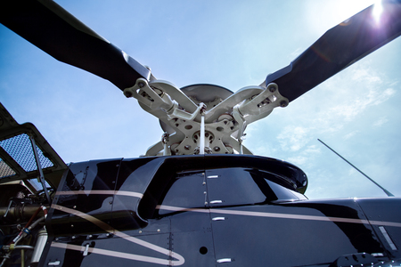 Close up of a screw of black with gray stripes bell 407 helicopter standing on green grass field in blue sky background.