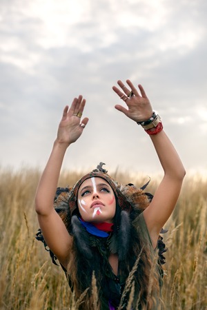 Beautiful girl model dressed in native American Indian clothes, with paint face camouflage and...
