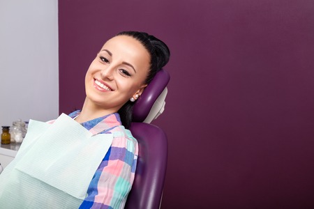Young woman patient in checkered shirt with perfect straight white teeth waiting for dentist in...
