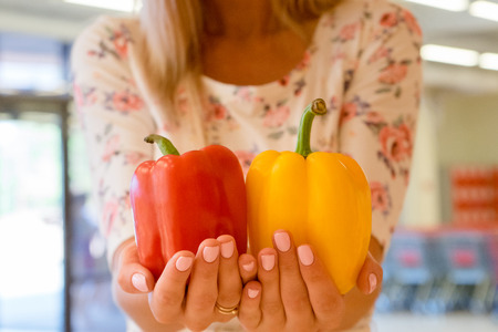 A girl holding two pepper in hand. Your choice of red and yellow. Fresh vegetables in the supermarket for salads and vegetearians. Living healthy foodの写真素材