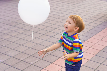 Little boy playing with a balloon. He runs down the street, laughing. Summer evening.の写真素材