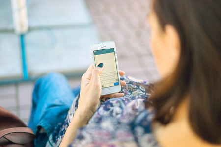 A pregnant woman is holding a phone in his hand. She sits on a bench and looking at the phone, typing text.の写真素材