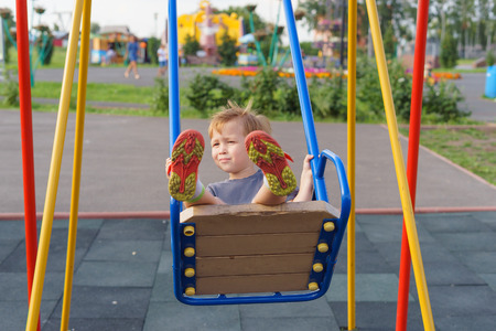 Boy swinging on a swing in the playground. A warm summer evening, children activities.の写真素材