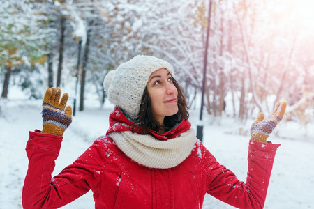 The girl looks at the sky with indignation. It's snowing, a young girl in a red coat, knitted cap and mittens, waiting for the snow from the sky. Dissatisfaction with the weather. Raised hands, gestures with hands apartの写真素材