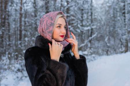 Young girl walking in winter forest, snowy evening, a girl dressed in a coat and a scarf on her head, make-up on her face. Siberian forest in the snow.の写真素材