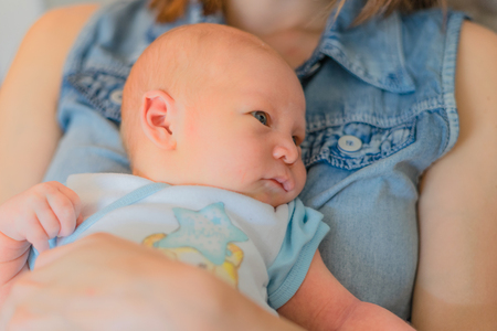 Mother holding baby in front of his, the boy is lying on mom's tummy. Newborn baby looking to the sideの写真素材