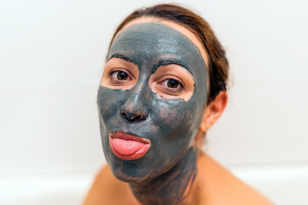 Mask of clay on the girl's face. Girl shows tongue. Wellness, nourishing and healthy clay healing mud. Wrinkle Facial.の写真素材