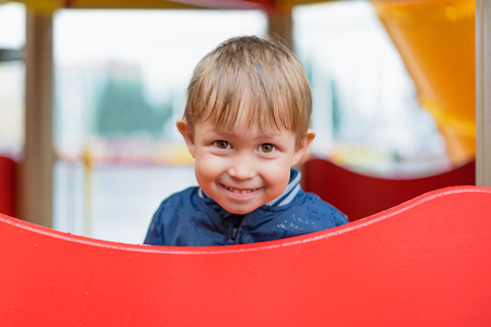 boy hiding from the rain on the playground. Shy child running around the playground.の写真素材