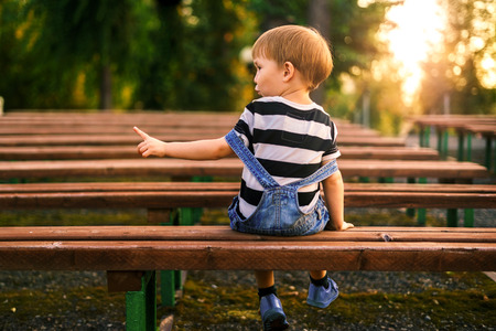 The boy points the direction with his hand to the left. The boy sits on a bench in the park and points to it with his finger. Summer Evening Sunsetの写真素材