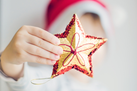 The child holds a toy star in his hand. Christmas tree decoration in a children's hand. A shiny Christmas star, a toy.の写真素材