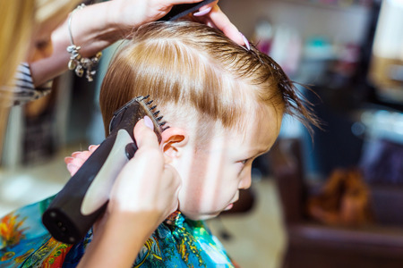 Haircut the machine. A little boy in a hairdresser. Female hand on headの写真素材