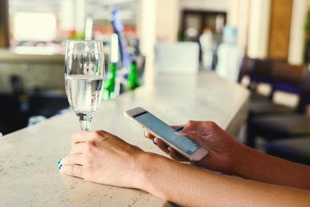 Girl at the bar with a glass of water. The girl with the phone in her hands and a glass of clean...