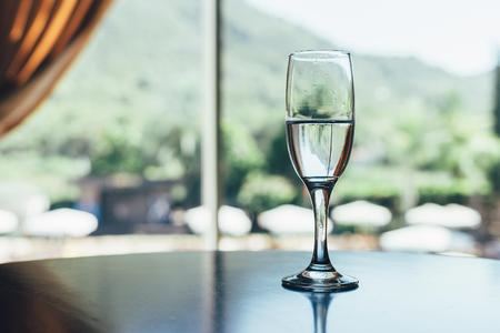 a glass of clean drinking water on the table. Crystal clear water in a glass. Large windows in the background, water reflection. Concept of drinking waterの写真素材