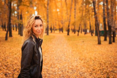 The girl walks through the autumn park. Brunette in a leather jacket in the forest. Yellow leaf...