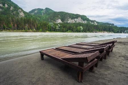 Wooden deck chairs at the fast mountain river. Rainy weather in the mountains