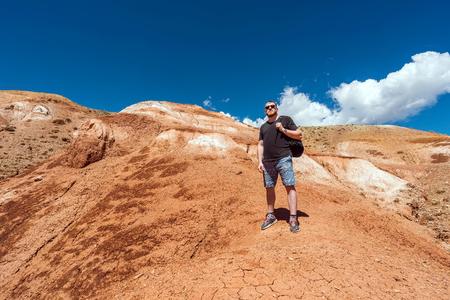 Tourist with a backpack goes up the hill. A man rises on a hill. Red mountains, sunny summer day.の写真素材