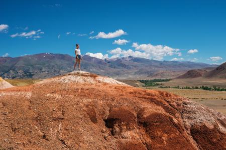 Girl tourist stands on the top of the mountain. Tourist on a high red hill. Landscape and travel to the mountainsの写真素材