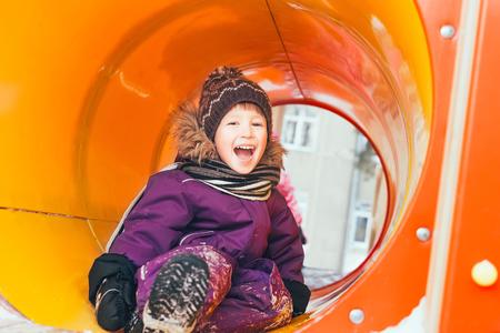 The boy plays on the playground in the winter. Cheerful baby is playing on the playground. Scarf, hat, gloves,の写真素材