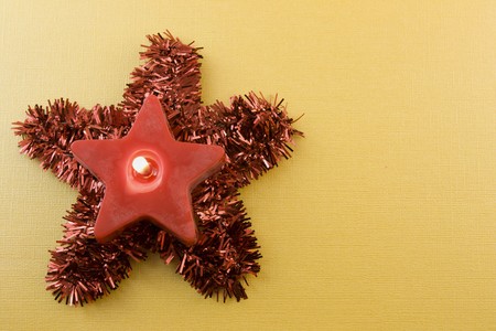 red Christmas star shaped candle on tinsel star with soft gold background and copyspaceの写真素材