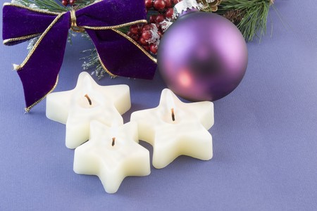 three Christmas star shaped candles with purple bauble, bow and copyspace