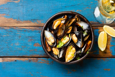 Mussels in clay bowl, glass of white wine and lemon on wooden blue backgroundの写真素材