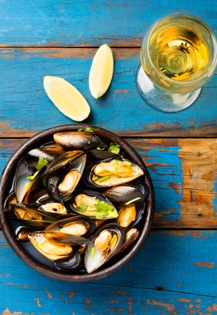 Mussels in clay bowl, glass of white wine and lemon on wooden blue backgroundの写真素材