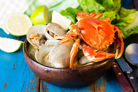 Seafood soup of clams and crab in clay bowl on wooden blue background.  Mariscal or paila marinaの写真素材