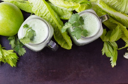 Two glasses of green smoothie and fresh green vegetables and fruits on black background. Top viewの写真素材