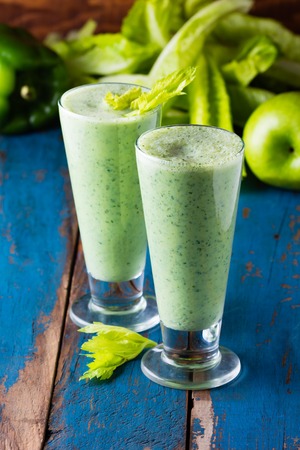 Two glasses of green smoothie and fresh green vegetables and fruits on wooden blue backgroundの写真素材