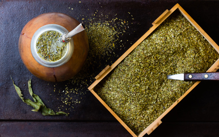 Yerba mate in calabash and dry herb in clay bowl on black background. Top view