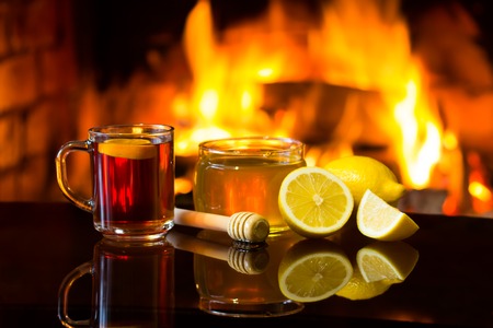 Cup of hot drink wine, bowl of honey and lemon in front of warm fireplace. Magical relaxed cozy atmosphere near fire.の写真素材