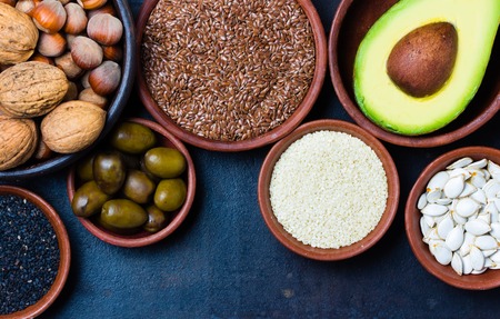 Vegetarian healthy fat sources on blck background. Nuts, avocado, olives, white and black sesame seeds, pumpkin seeds. Omega three and omega six oilsの写真素材