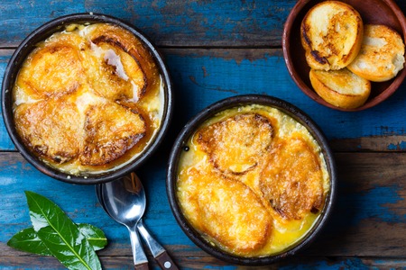 Onion soup with dried bread and cheese on clay bowls on wooden blue background. Top viewの写真素材
