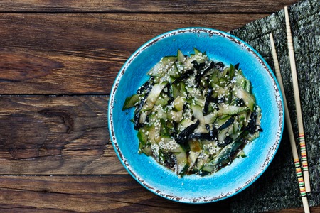 Asian food. Asian salad with seaweed nori, cucumber, white sesame seeds and soya in blue bowl on wooden rustic background. Top viewの写真素材